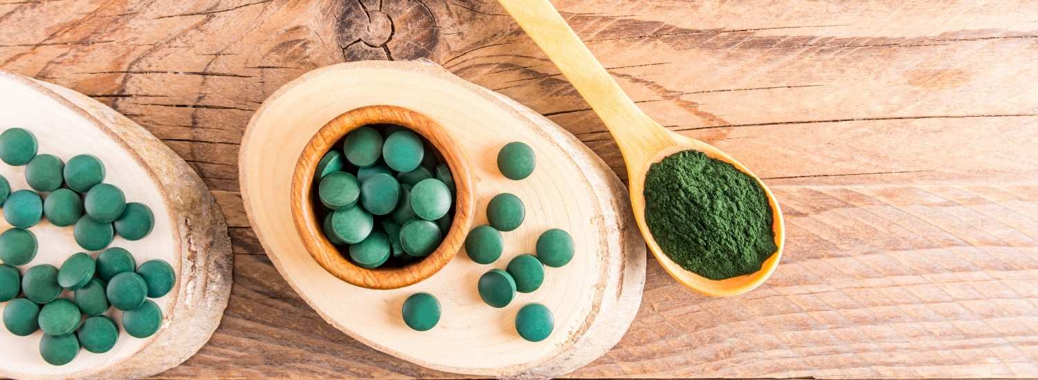 Des cachets de spiruline et de la poudre de spiruline disposés sur une table en bois