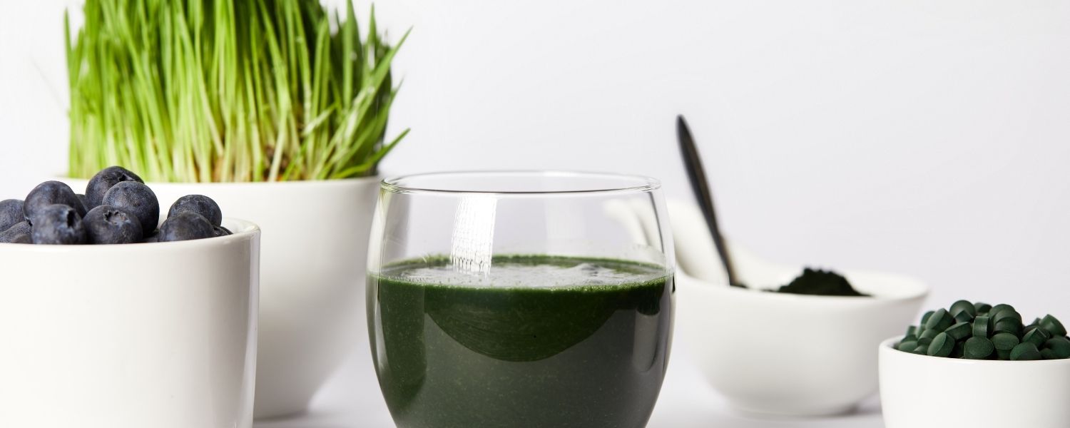 Un verre contenant de la spiruline en poudre diluée, posé à côté de bocaux de cachets de spiruline