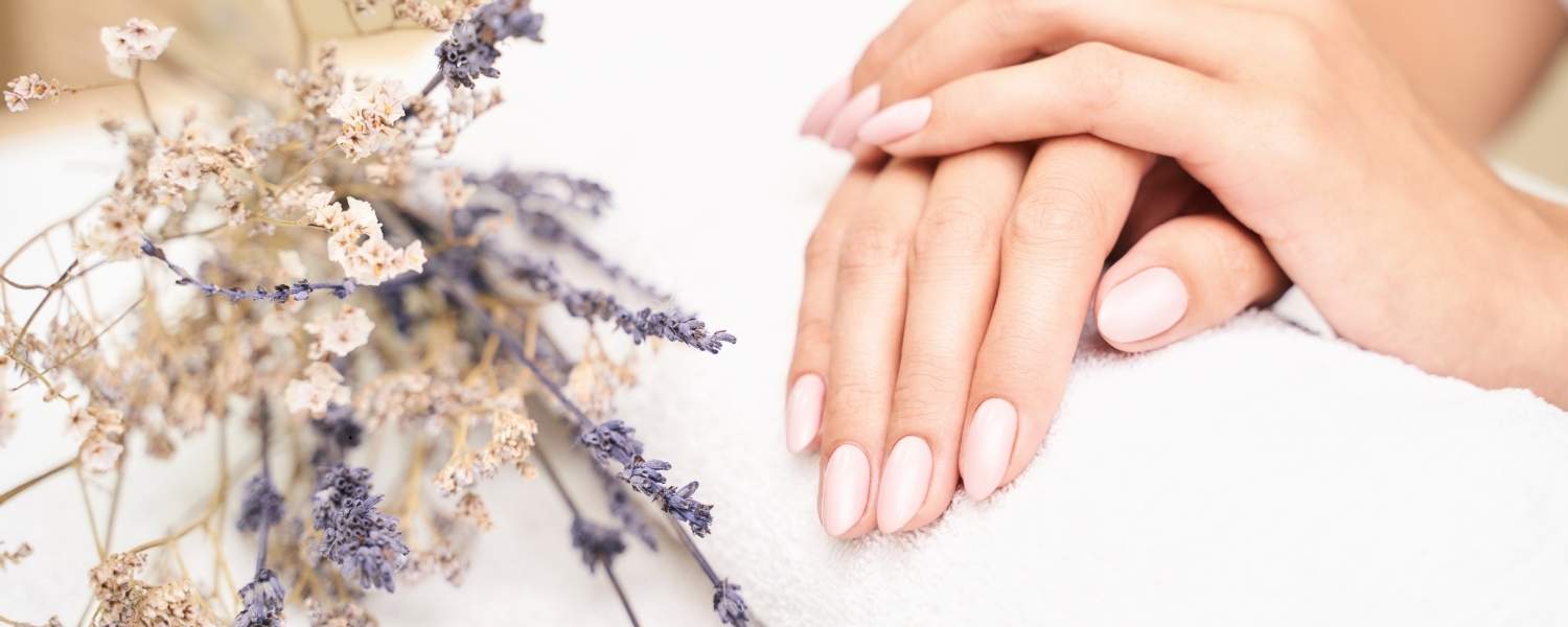 image représentant des mains aux ongles manucurés avec un vernis rose pâle, reposant sur une serviette blanche. 