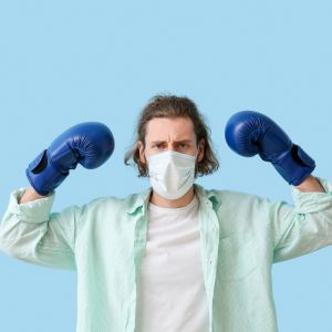 Un homme avec un masque chirurgical et des gants de boxe, se battant contre la maladie