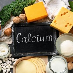 Aliments riches en calcium, tels que le fromage, les noix, les légumes verts et les produits laitiers, entourant une ardoise avec l'inscription 'Calcium'