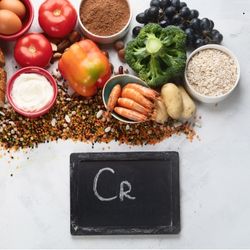 Aliments sources de chrome, comme les légumes, fruits, céréales, et crevettes, autour d'une ardoise indiquant 'Cr'