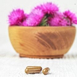 Capsules marron devant un bol en bois rempli de fleurs violettes de chardon-Marie.