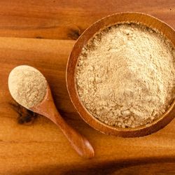 Poudre de maca dans un bol en bois et une cuillère, posée sur une table en bois.