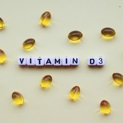 Des capsules d'huile jaune dispersées sur une surface claire, avec des lettres formant "Vitamin D3" au centre.