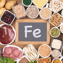 Sources alimentaires de fer, incluant des viandes, légumes secs, céréales et légumineuses, autour d'une ardoise marquée 'Fe'.