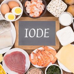 Aliments riches en iode, comme les fruits de mer, poissons, œufs et produits laitiers, entourant une ardoise marquée 'Iode'.