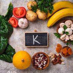 Aliments riches en potassium, comme les bananes, les pommes de terre, les épinards et les fruits secs, disposés autour d'une ardoise marquée 'K'