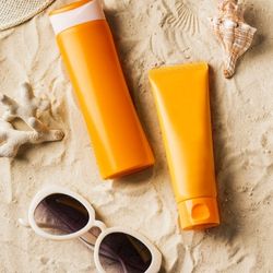 2 tubes de crème solaire et une paire de lunette de soleil posés dans le sable