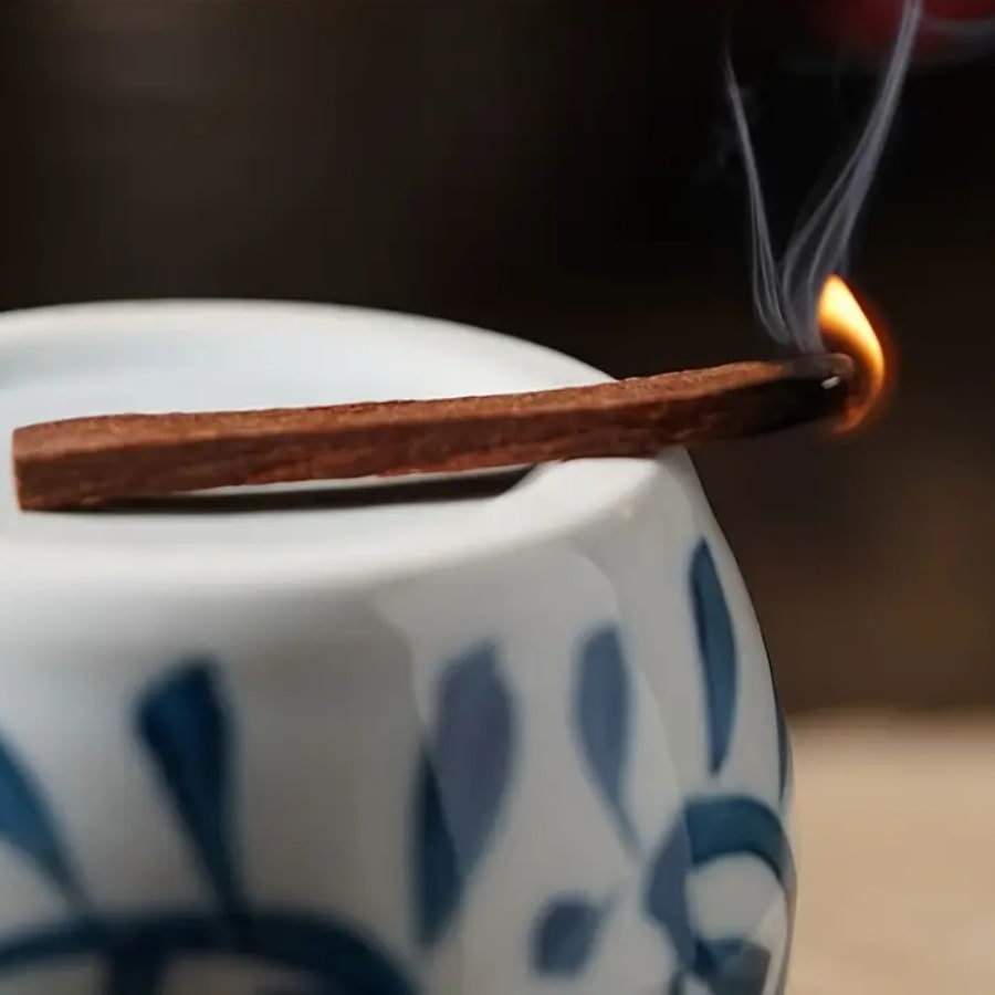 Un Bâtonnet de Bois de Palo Santo Parfumé au Bois de Santal en train de e consumer dans un brûleur en céramique