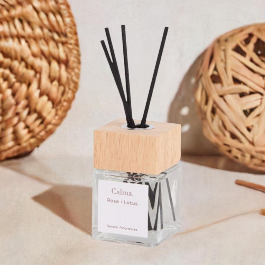 Un Diffuseur de parfum à bâtonnets senteur Rose & Lotus, devant un panier en osier et un plateau en osier