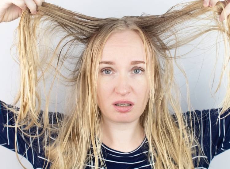 Une femme ayant l'air dépité en se tenant ses cheveux visiblement très gras