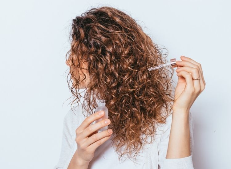 Photo d'une femme aux cheveux bouclés en train de s'appliquer un soin capillaire, à l'aide d'une pipette