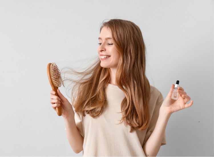 Photo d'une femme avec des cheveux long, une brosse en main gauche et un complément en main droite, ayant l'air heureuse de sa longue chevelure. 